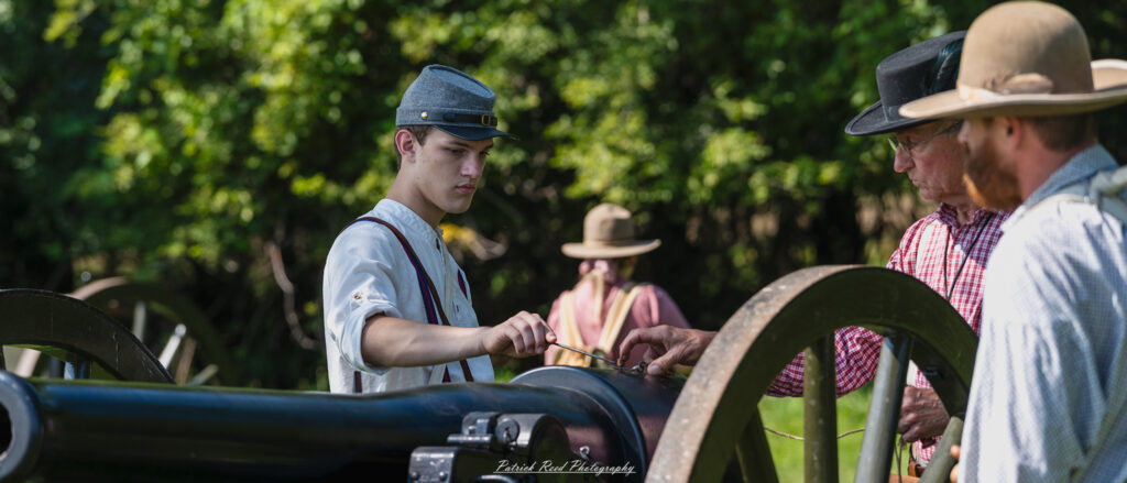 A soldier preparing a cannon to fire, carefully loading it with ammunition. Dressed in a military uniform, he demonstrates focus and precision as he checks the cannon's readiness, surrounded by fellow soldiers who assist in the operation. The scene captures the urgency and camaraderie of artillery preparation on the battlefield.
